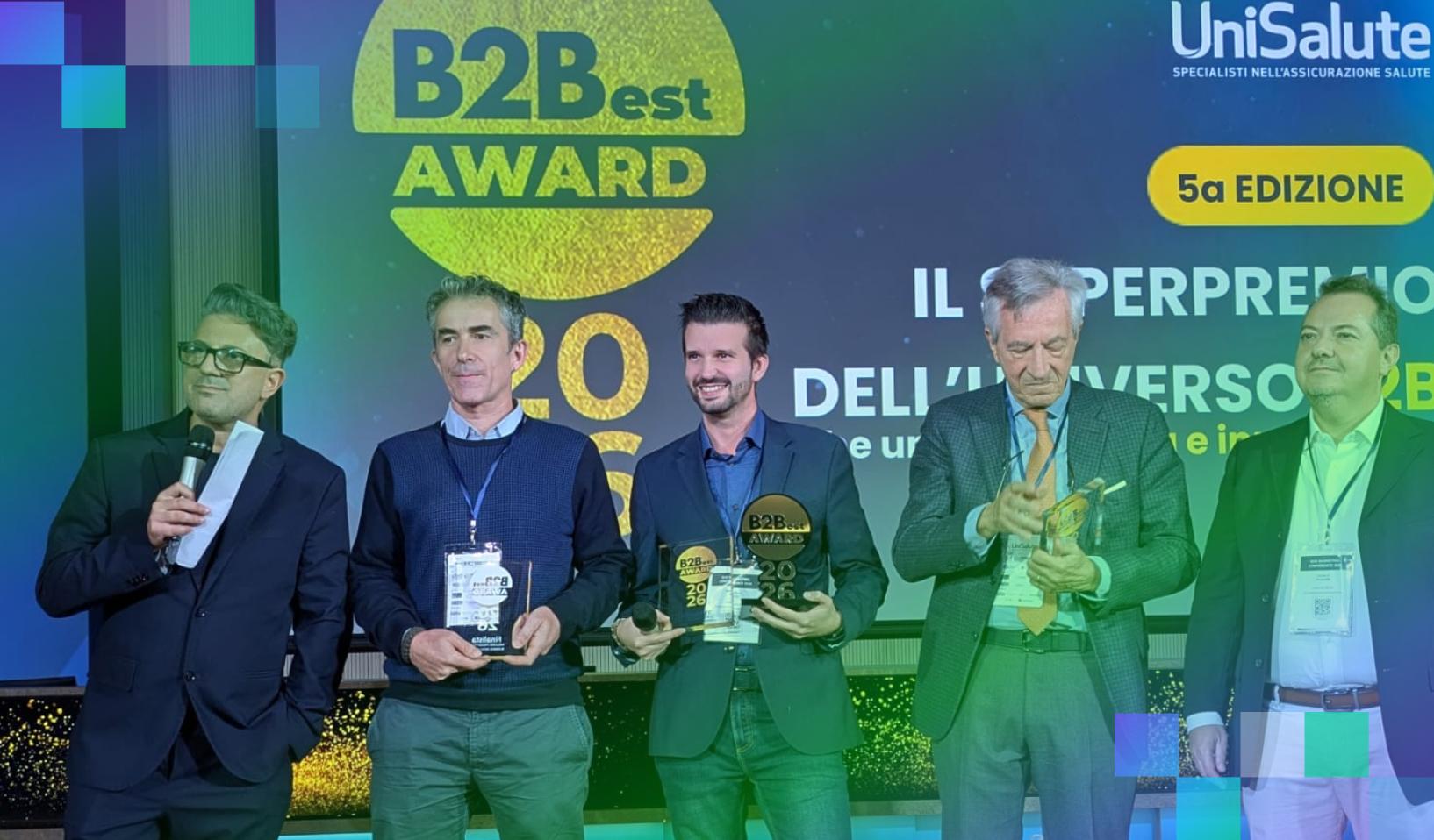 Cinque uomini sul palco durante la premiazione del B2Best Award, alcuni con i trofei in mano, davanti allo schermo con il logo dell’evento.